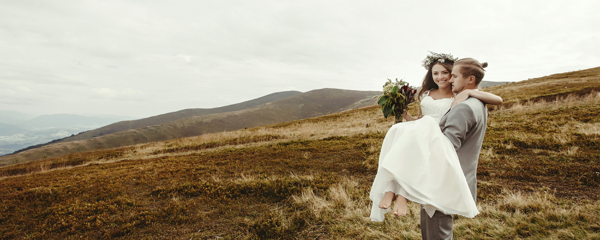 groom carrying bride over an open field 